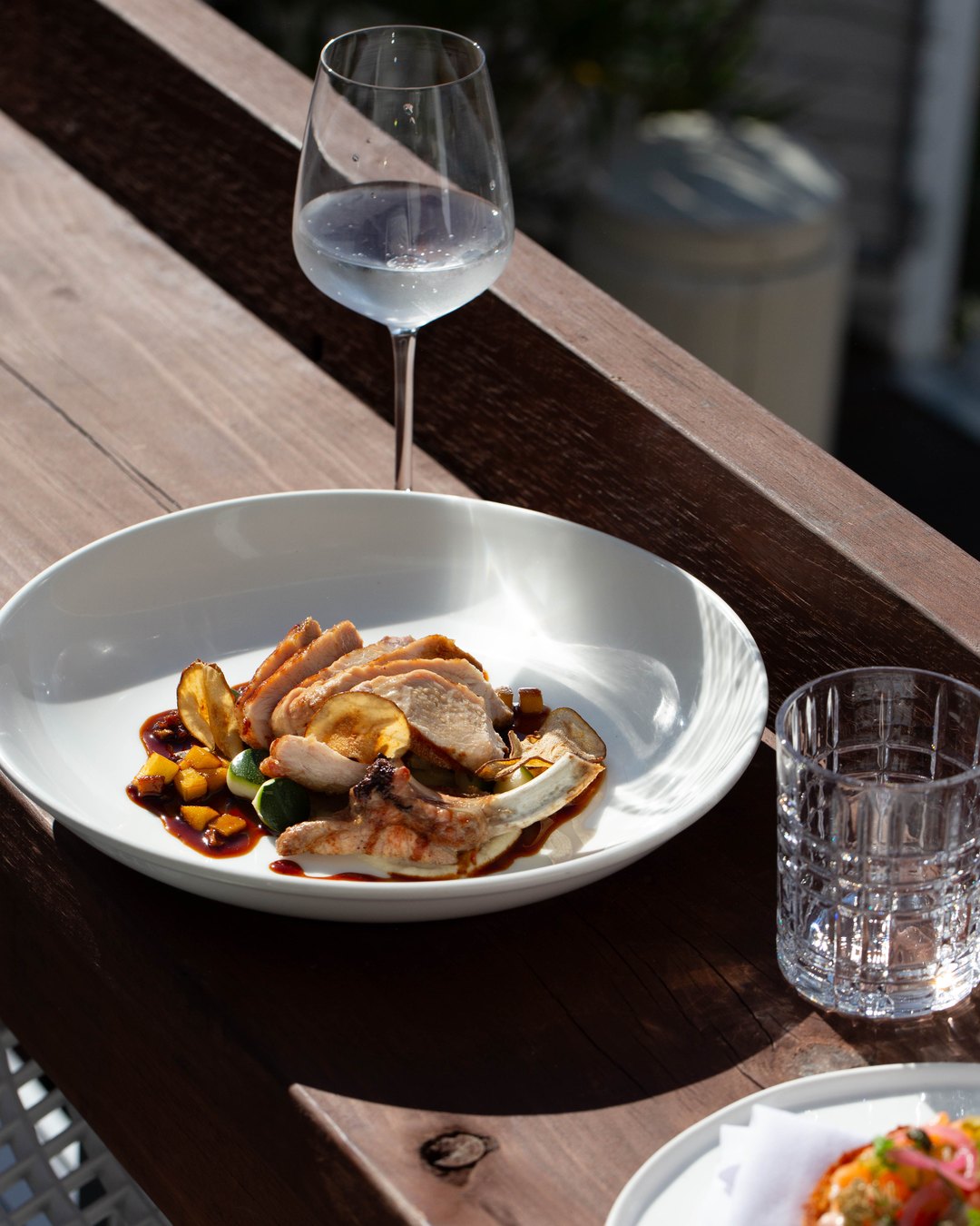 A glass of white and the pork cutlet on the deck rail